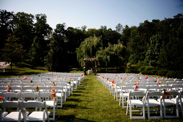outdoor ceremony with white chairs and floral accents - grass aisle -  charming Hudson Valley NY wedding photo by top New York wedding photographers Belathee Photography